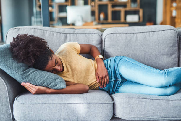 Tummy pain might be trying to tell you something Shot of a young woman experiencing stomach pain while lying on the sofa at home hernia photos stock pictures, royalty-free photos & images
