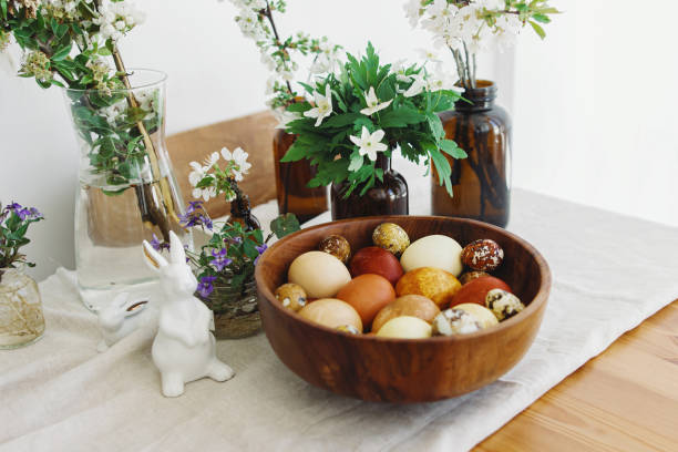 istock Stylish easter eggs in wooden bowl on rustic table with bunny and blooming flowers. Happy Easter! 1306633879