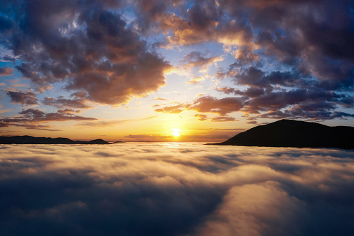 Beautiful sunrise in the mountains. Scenic landscape with dramatic sky over thick clouds in mountain valley. Aerial drone view.