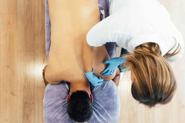 vista dall'alto di un trattamento in una clinica di fisioterapia. fisioterapista femminile che esegue un trattamento di accostamento secco sulla schiena nuda di un paziente nel dolore. - shirtless male men people foto e immagini stock