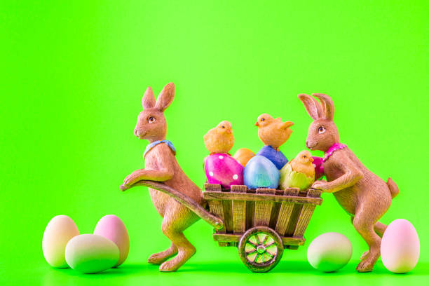 istock Two Easter bunnies and a cart with lots of colorful Easter eggs and chicks 1306647633