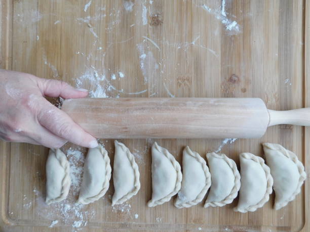 istock Front view of woman's hands making meat dumpling with wooden rolling pin. 1306648901