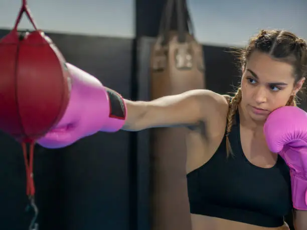 Photo of Boxer girl with pink boxing gloves working out with an uppercut punching bag on a gym.