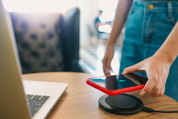istock Charging mobile phone battery with wireless device in the table. Smartphone charging on a charging pad. Mobile phone near wireless charger. 1306649610