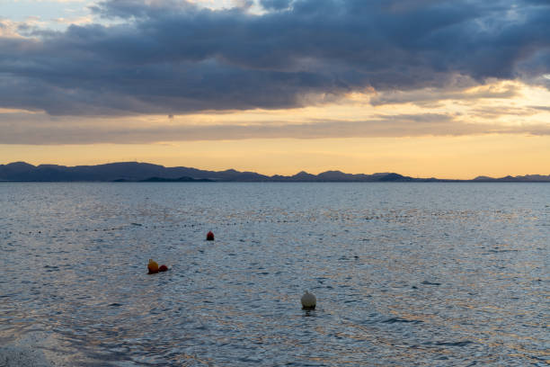 View of calm ocean waters under an expressive sky at sunset with mountain silhouette in the background and buoys in the foreground