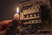 Men in complete darkness holding a candle to investigate a home fuse box during a power outage. Blackout concept.