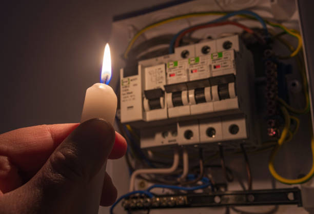 Men in complete darkness holding a candle to investigate a home fuse box during a power outage. Blackout concept. stock photo