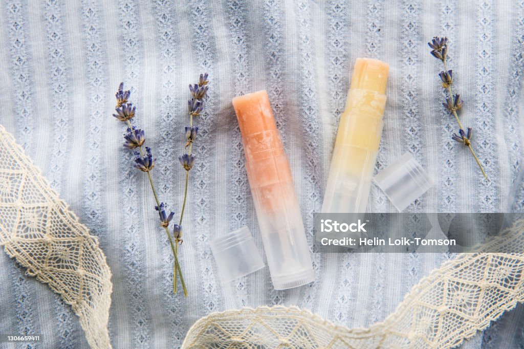 Make homemade natural organic ingredients lip balm. Handmade lip balm and lipstick inside container on boho vintage blue textile cloth background and dried lavender flower for decoration. Lip Balm Stock Photo