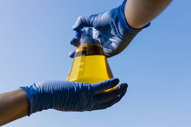 mano con guantes sosteniendo vaso de precipitados con biocombustible de etanol contra el cielo azul - e85 fotografías e imágenes de stock