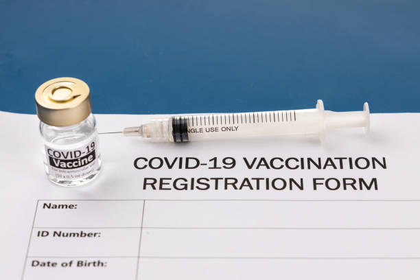 istock Covid-19 vaccination registration form with vial and syringe on blue desk 1306662080
