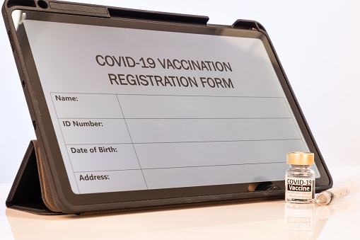 Covid-19 vaccination online registration form on computer tablet screen with vial and syringe as props on table top