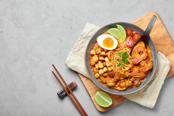 laksa en tazón gris en la parte superior de la mesa de hormigón. sopa de fideos de coco con carne de pollo y gambas de cocina peranakan. comida asiática. - coconut milk soup fotografías e imágenes de stock