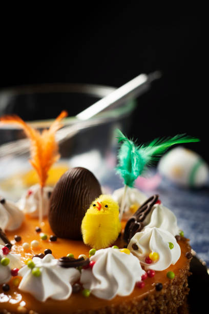 mona de pascua, eaten in Spain on Easter Monday closeup of a spanish mona de pascua, a cake eaten on Easter Monday, ornamented with a plush chick, a chocolate egg and feathers of different colors, on a table easter cake stock pictures, royalty-free photos & images