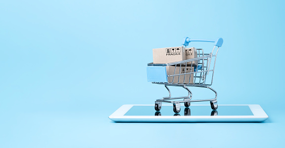 Aislado de cajas de papel de envío dentro de carro de la compra azul en tableta con fondo azul y espacio de copia, compras en línea y concepto de comercio electrónico. photo