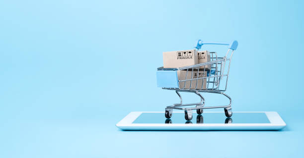 青い背景とコピースペース、オンラインショッピング、電子商取引のコンセプトを持つタブレット上の青いショッピングカートトロリー内の出荷紙箱の分離。 - eコマース ストックフォトと画像