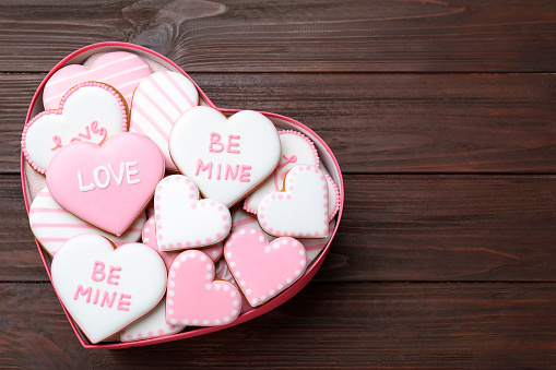 Valentine's day cookies in heart shaped box on wooden table, top view. Space for text