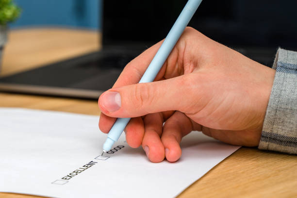 istock A questionnaire with answer options for the feedback form. A man ticks a box on a white paper while sitting at a wooden table. Checking the form of the check box. 1306670466