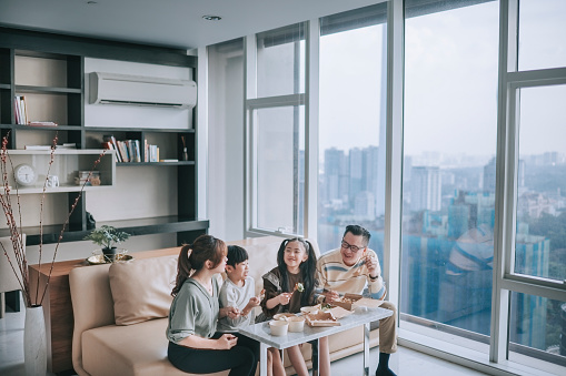 asian chinese young family enjoying take out food in front of tv in living room during weekend