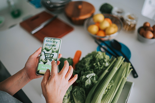 Online shopping mobile app holding by asian chinese housewife in front of kitchen counter