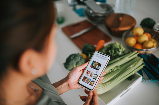 Vista de gran angular de la mano de la mujer china asiática en la aplicación móvil para la entrega de alimentos en línea frente al mostrador de la cocina photo