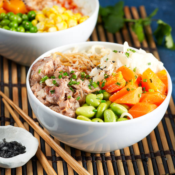 istock Two assorted poke bowls, pulled pork, vegetables, pumkin, soy beans edamame, noodles, on bowl, chopsticks. blue dark background. Closeup. Trendy asian food. Healthy, clean eating concept. 1306680656