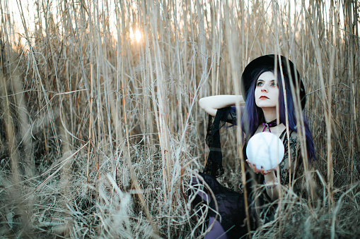 Violet hair died female witch in the field with white moon globe ball