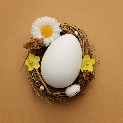 Easter background. White Easter egg in a nest basket on a beige background. Square photo.