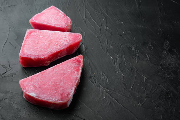 istock Raw frozen tuna fish fillet, on black stone background , with copyspace  and space for text 1306688832