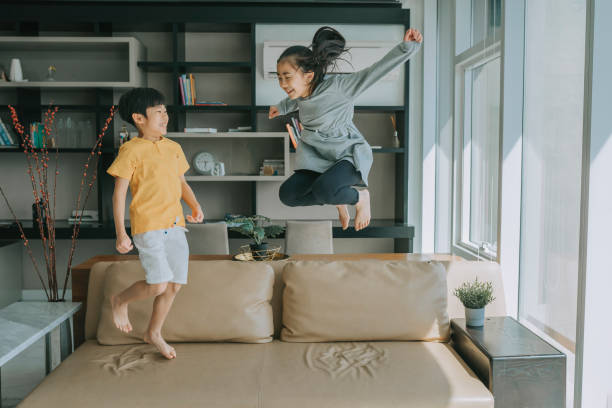 アジアの中国の若い男の子と女の子が楽しそうにソファのソファに飛び乗る - domestic life jumping child sofa ストックフォトと画像