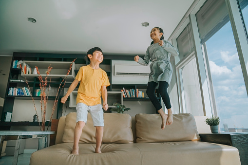 asian chinese young boy and girl jumping on the couch sofa happily