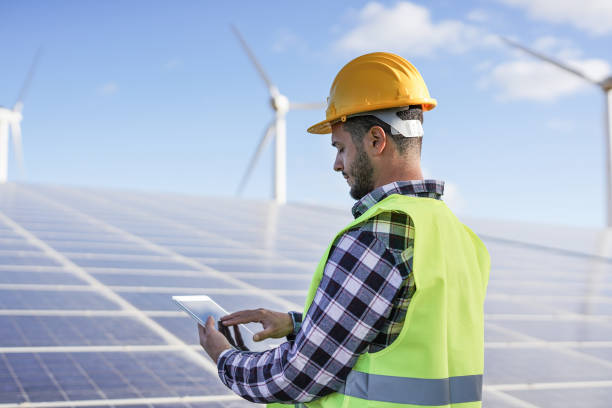 istock Young man working at solar power station with digital tablet - Renewable energry with wind turbines and solar panels 1306693007
