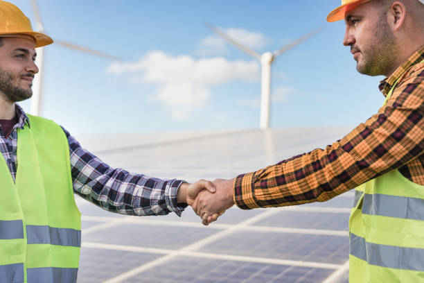 istock Men shaking hands at solar power station - Renewable energy concept with solar panel and wind tubine 1306693021