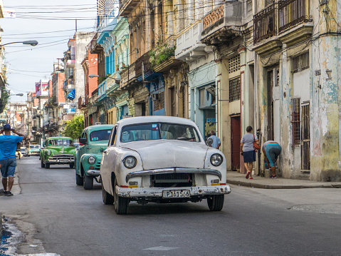 Havana, Cuba-December 2017: Authentic view and atmosphere on the streets of Havana. Cuban car driving true the neighbourhood filled up with local people and colonial residences in the background.