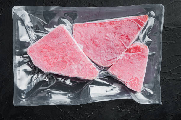 pacchetto sottovuoto di bistecca di tonno congelata, su sfondo in pietra nera, laici piatti con vista dall'alto - tuna seared tuna steak prepared ahi foto e immagini stock