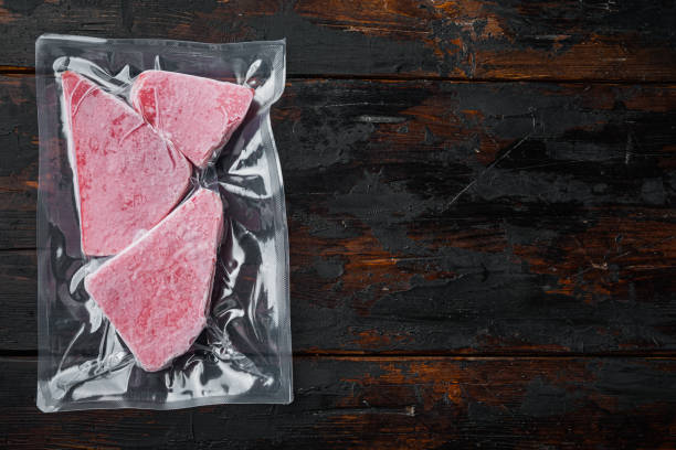 진공 플라스틱 패키지에 냉동 참치 생선 스테이크, 오래된 어두운 나무 테이블 배경에, 상단 보기 평면 누워, 카피 스페이스와 텍스트 공간을 가진 - tuna prepared ahi food tuna steak 뉴스 사진 이미지