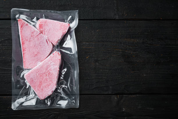 pacchetto sottovuoto di bistecca di tonno congelata, su sfondo nero in legno, lay piatto con vista dall'alto, con spazio di copia e spazio per il testo - tuna seared tuna steak prepared ahi foto e immagini stock