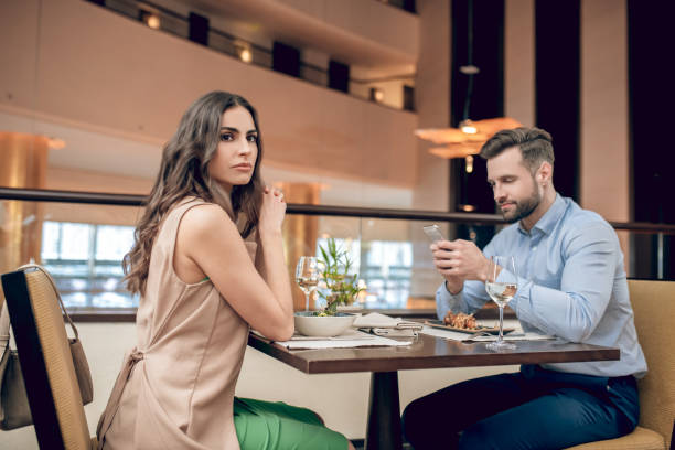 um casal sentado à mesa no restaurante e mulher olhando sem flexibilidade - women heterosexual couple love men - fotografias e filmes do acervo