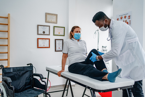 Therapist treating injured knee of athlete male patient in clinic