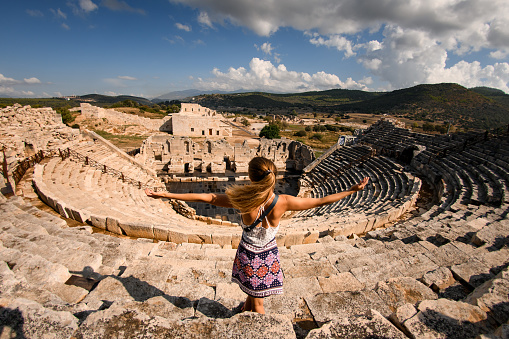 beautiful woman with raised hands at ruins of the ancient Lycian city Patara. Amphi-theatre and the assembly hall of Lycia public.