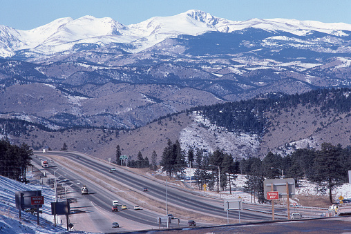 Just outside of Denver, nestled in the foothills of the Colorado Rockies looking west, Interstate 70 snakes its way onward and upward through the Rocky Mountains.  Snow covered peaks are seen in the background.