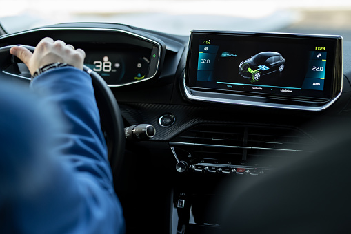 Tallinn, Estonia - February 19 2021: New Peugeot e 208 2020 control display. Electric car interior. Woman hand holding steering wheel. Selective focus.