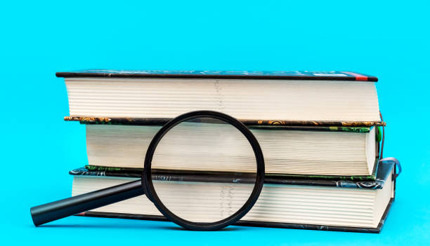 istock Magnifying glass and stack of books on blue. 1306708729