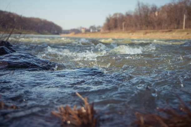 Water texture. Mountain river on the background of the city. Waves of green, blue and gray. Calm and tranquility. River shore. Rapid flow of water, photo of the surface of the river