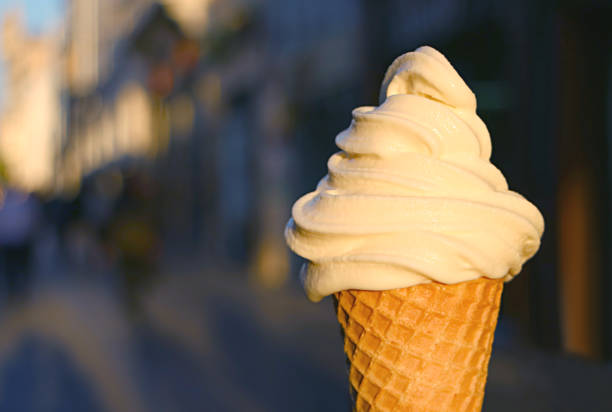 closeup vanilla soft serve ice cream cone with blurry walking street in background - soft serve ice cream photos et images de collection