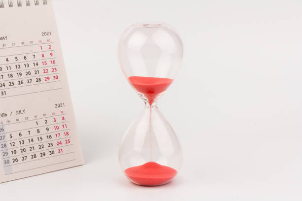 istock Time passing concept. Crystal hourglass with red sand and calendar on light background 1306714860