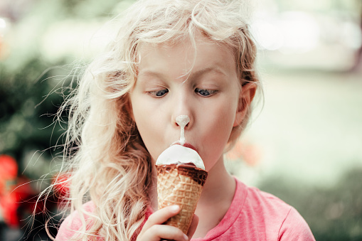 Cute funny adorable girl with dirty nose eating licking ice cream. Kid looking at food with crossed eyes. Hilarious child eating tasty sweet cold summer food outdoor. Summer fun.
