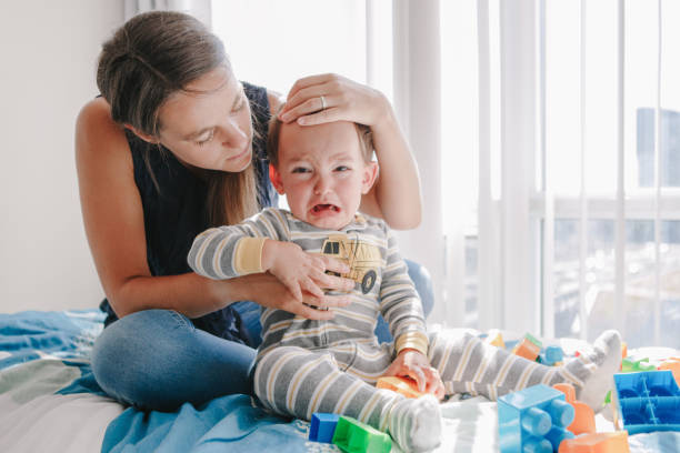 mother hugging pacifying sad upset crying toddler boy. family young mom and crying baby sitting on a bed at home. bonding relationship of mom and child baby. family together protection. - criança de 1 a 2 anos imagens e fotografias de stock