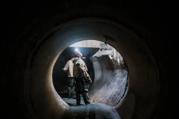 Sewer tunnel worker examines sewer system damage and wastewater leakage.