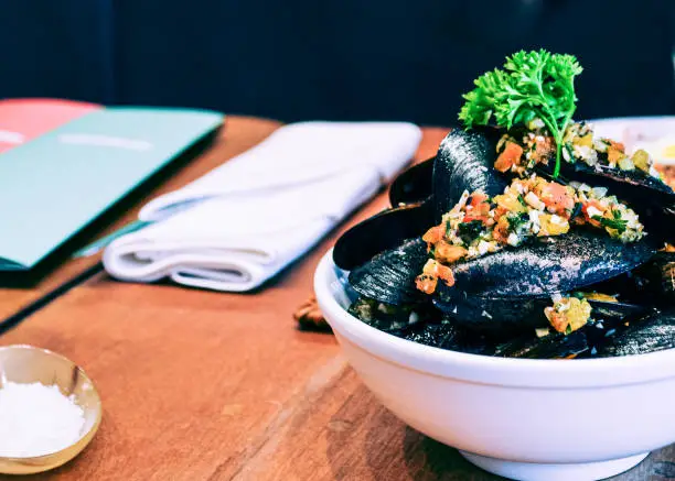Stream mussel in white bowl garnish with chopped tomato and pepper in olive oil dressing decorative with parsley.