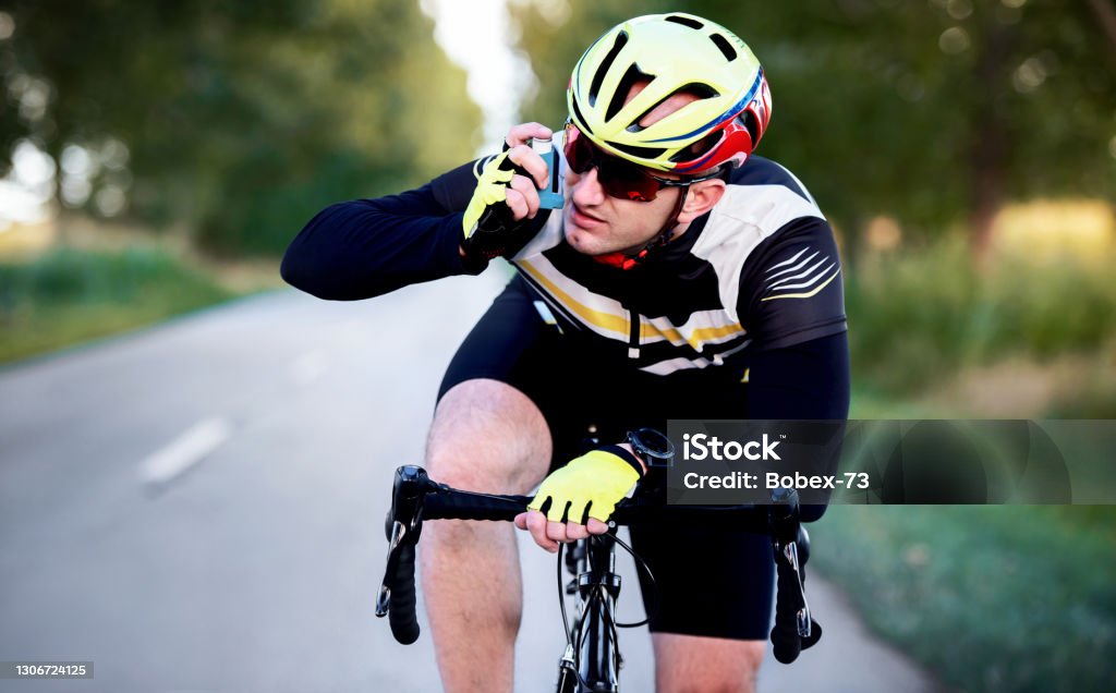 Sports and asthma. Cyclist using asthma inhaler while riding a bicycle. Sport and recreation concept Asthma Inhaler Stock Photo